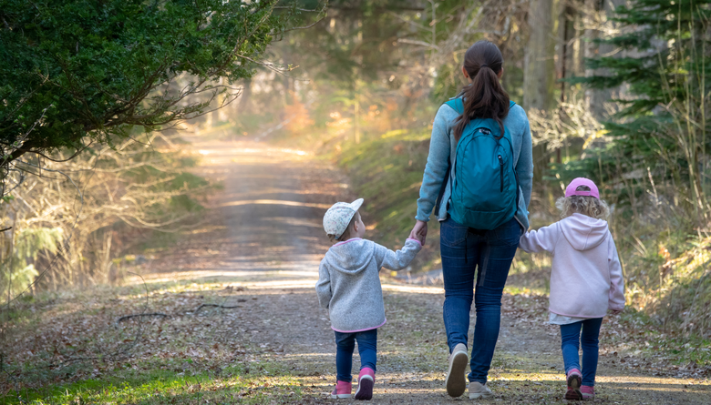 Hiking in the woods. Mother with daughters walking on a path in a sunny forest. Sweden